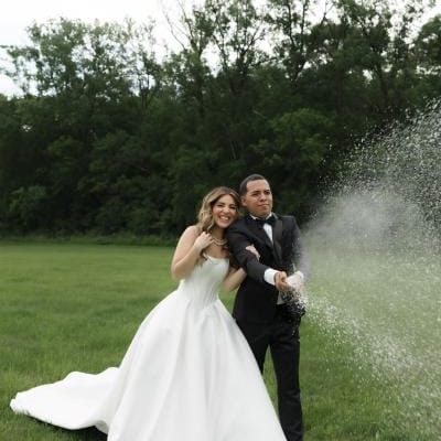 Bride and groom stand on lush grounds of Belle Âme Vineyard, sparying champagne to celebrate their wedding day