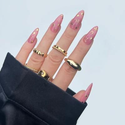 Hand peeking out of sweatshirt sleeve, with Deco Beauty nail sticker manicure and gold rings on fingers