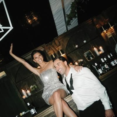 Bride poses on the bar in her sparkly after party attire with the groom by her side at Milwaukee Country Club