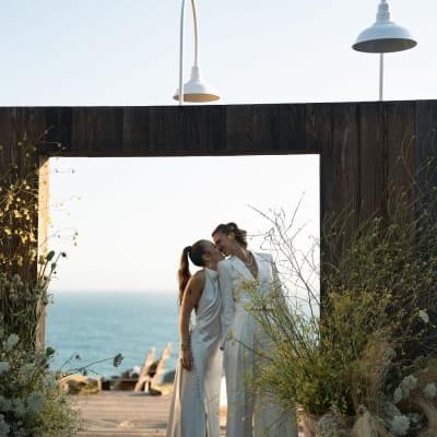 Couple shares a kiss in outdoor door frame, framed by yellow wildflowers and the sea in the background at The Sea Ranch Lodge