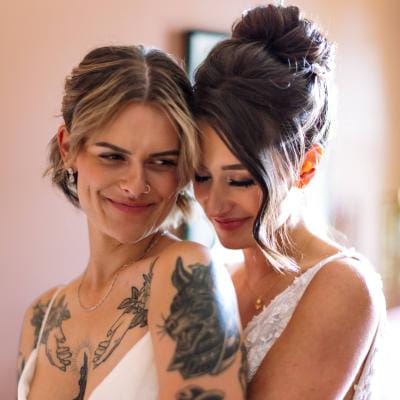 Couple holds each other in their arms, both wearing gorgeous wedding dresses during their first look