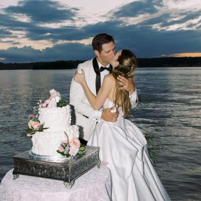 Bride and groom share a kiss during lakeside cake cutting as the sun sets on Pewaukee Lake