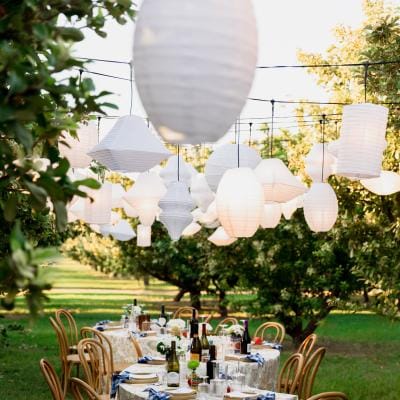 Serpentine table embrace an Italian aesthetic with paper lanterns hanging overhead in imagined backyard wedding on a private orchard