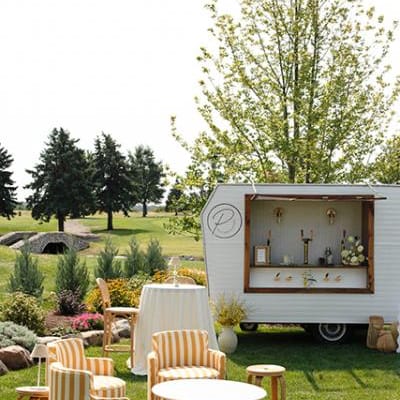 Sunny outdoor happy hour scene with yellow striped furniture and mobile bar at the Wexford at Emerald Greens