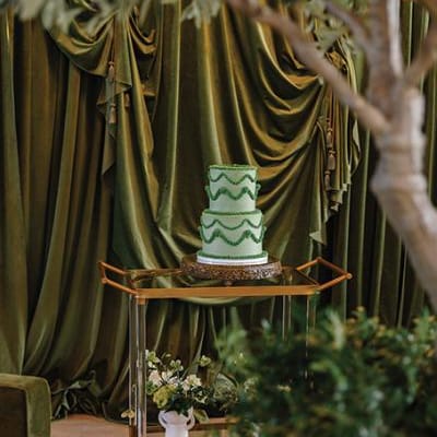 Green lambeth-style cake framed by greenery against a backdrop of dramatic green velvet draping at Westlin Hall