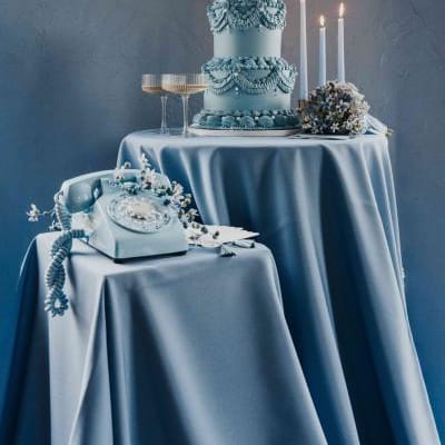 Dusty blue styled scene featuring After The Tone phone, two-tiered lambeth cake, candles and two glasses of champagne on silky tablecloths