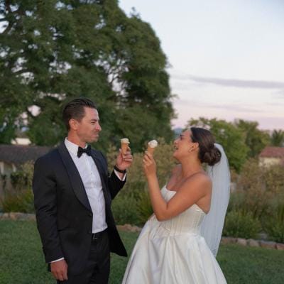 Bride and groom eat from ice cream cones on the ground of their outdoor wedding
