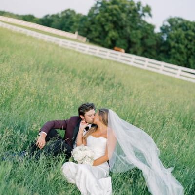 Bride and groom sit and share a kiss in a field on a private estate 