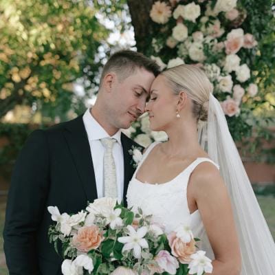 Bride and groom stand with foreheads pressed together, the bride holding her bouquet at their outdoor wedding day