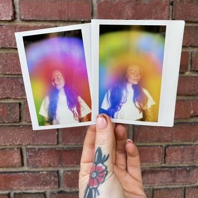 Two physical aura photograph polaroids by Vivid violet Aura side by side against a brick wall
