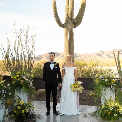 Bride and groom stand hand in hand at the altar, framed by bright blooms and cacti at The Willow Weddings & Event Center