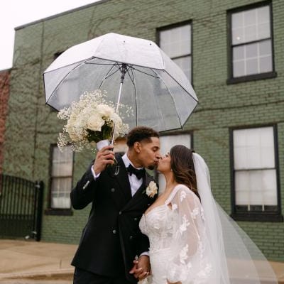 Bride and groom share a kiss under a clear umbrella outside of The Ivy House
