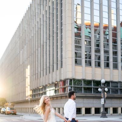 Katie and Zachary cross a street in Downtown St. Paul in their engagement photo session 