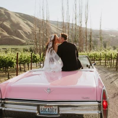 Lauren and Braedon share a kiss as they sit in a classic pink cadillac convertible