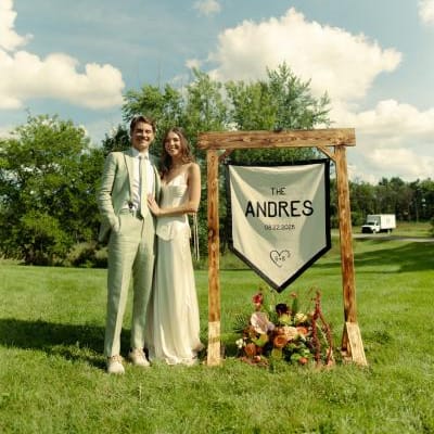 Sara and Billy stand by their custom made "Camp Andres" sign on their wedding day 