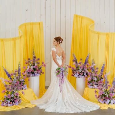 Model poses at altar with yellow fabric structures and lavender florals