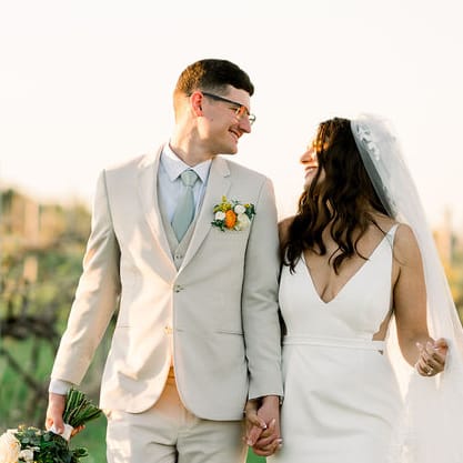 Bride and groom smile at each other while walking through the grounds of Bella Terre Vineyard during golden hour