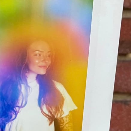 Two physical aura photograph polaroids by Vivid violet Aura side by side against a brick wall