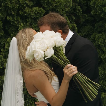 Sadie and Charlie share a kiss, hidden by a white rose bouquet