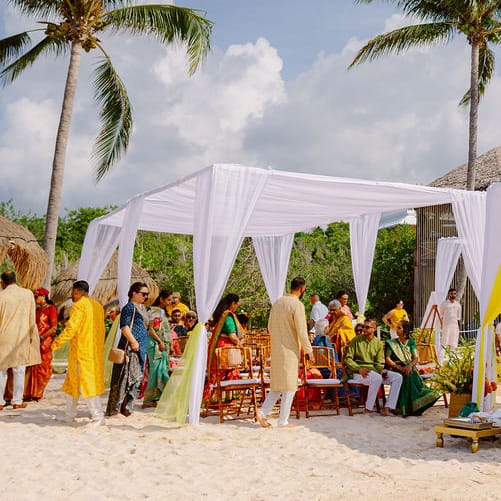 Outdoor multicultural ceremony featuring bright yellow draping on the beach
