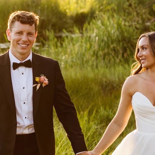 Bride and groom walk hand in hand in the golden hour light on the grounds of Sunriver Resort