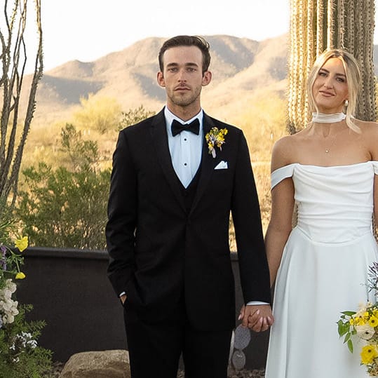 Bride and groom stand hand in hand at the altar, framed by bright blooms and cacti at The Willow Weddings & Event Center
