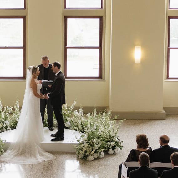 Bride and groom standing at the altar against a backdrop of floor-to-ceiling windows at Lumber Exchange Ballrooms