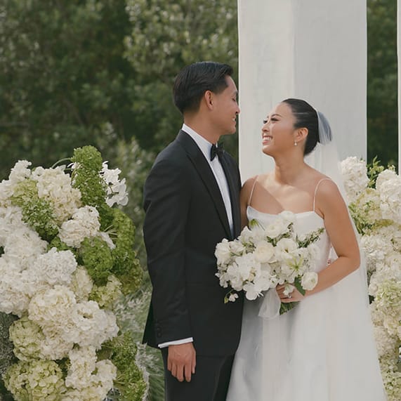 Bride and Groom smile at each other in front of modern altar surrounded by lush organic florals