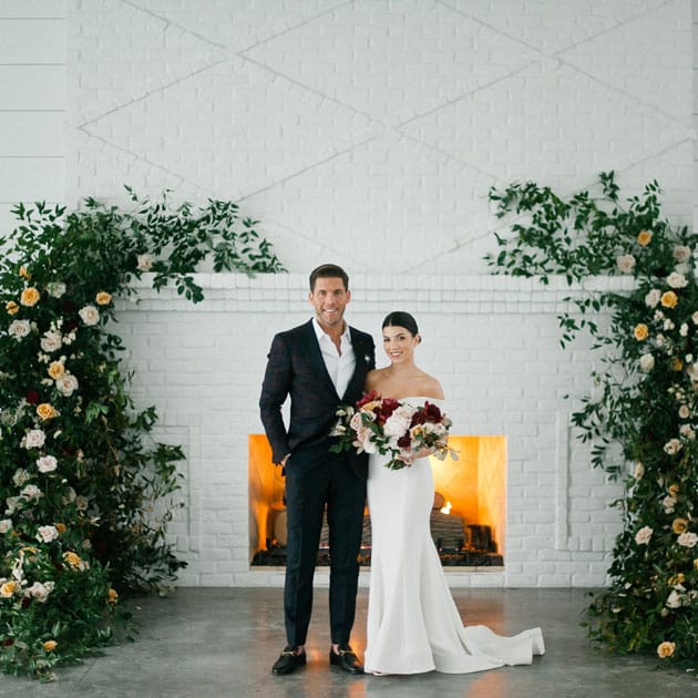 Sydney and Casey pose before the beautiful fireplace and their rosy floral installation at Hutton House