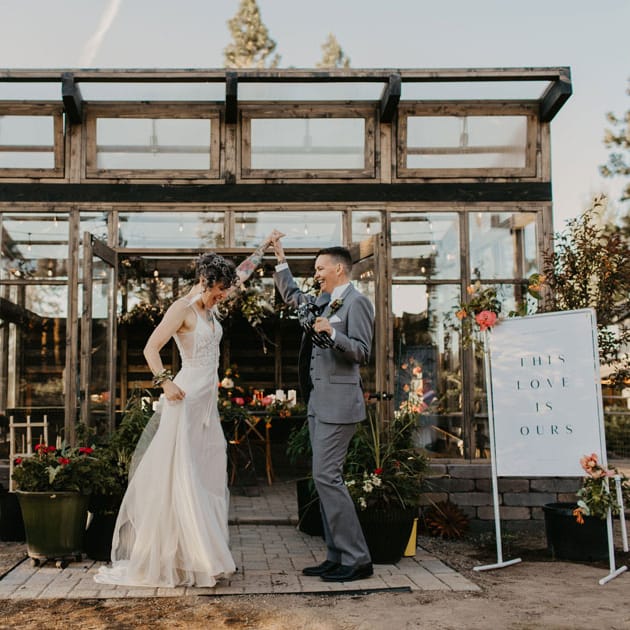 The couple stands outside a greenhouse overflowing with local blooms.