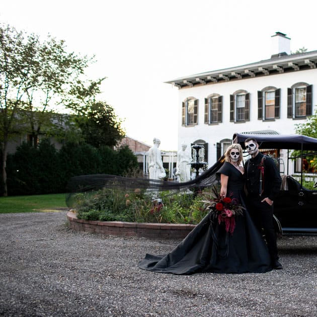 The bride and groom stand before their carriage at Maxwell Mansion in their Halloween wedding attire.