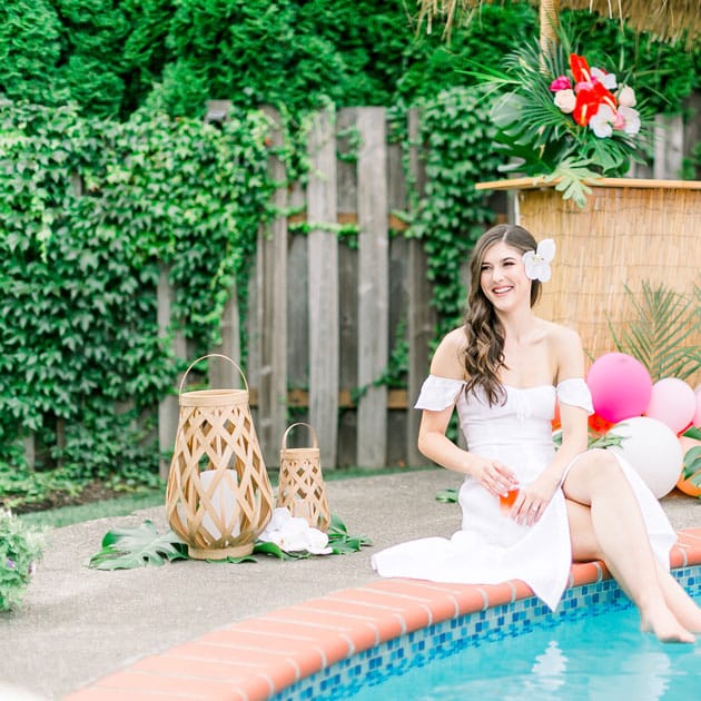 The bride relaxes in the pool near a balloon installation with a drink in hand.