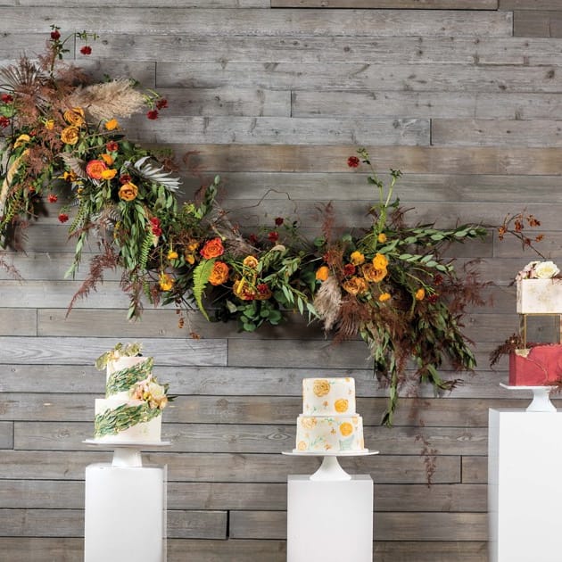 A playful installation of ranunculus, roses, olive branches and ferns frolics across the wall behind an array of autumn-inspired cakes at Machine Shop.