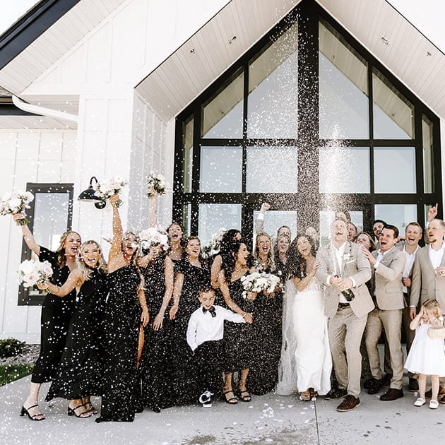A full wedding party cheers as they pop a bottle of Champagne in Woodhaven in Cannon Falls, Minnesota