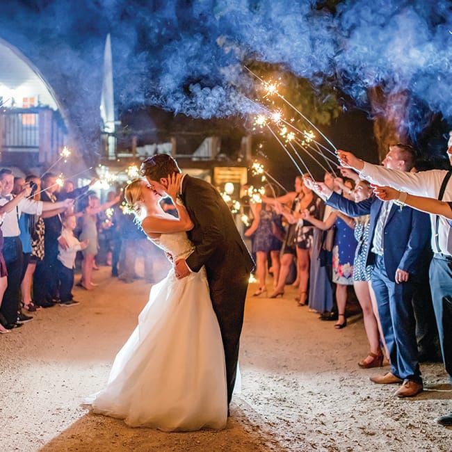 Family and friends hold sparklers as Taylor and John kiss as their wedding day at Historic John P. Furber Farm ends.