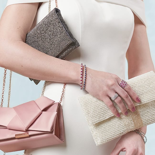 A bride holds three different bridal clutches: pewter, pink and ivory.