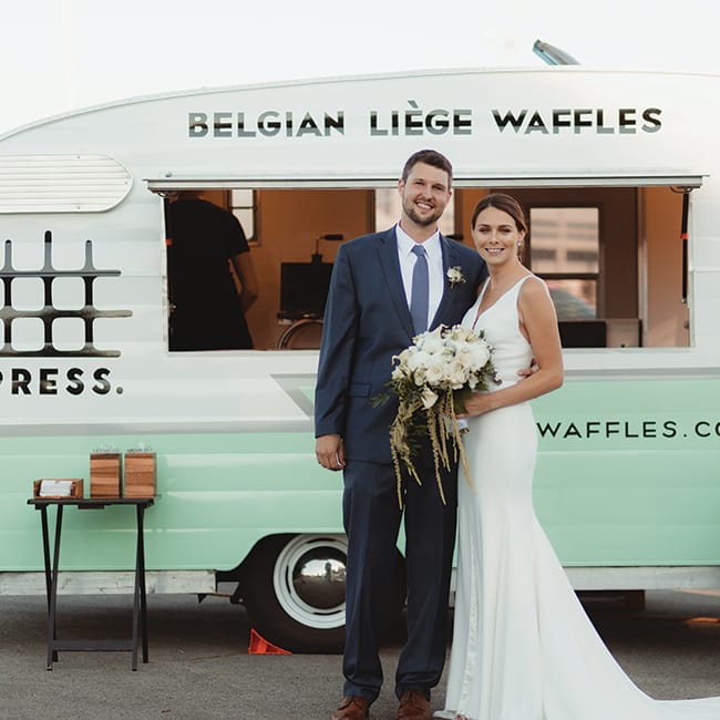 A couple stands in front of Belgian Liege Waffles, part of a new wedding trend: food stations.