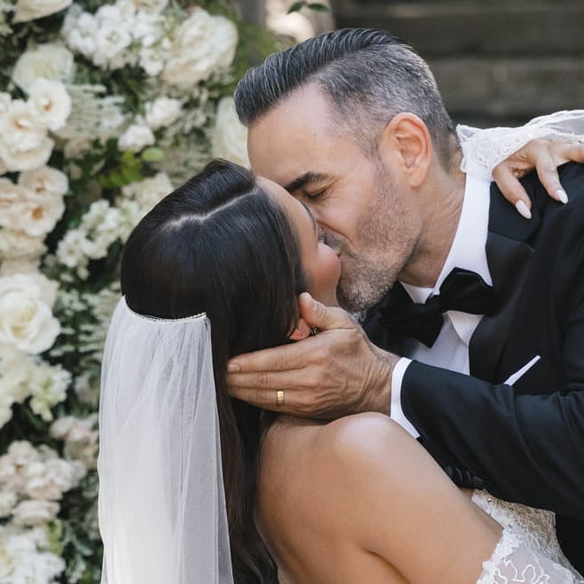 Bride and groom seal their vows with a kiss framed by an arch of lush white florals