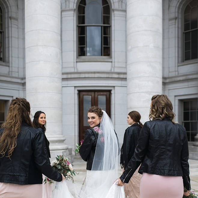 Jayme Udvare looks back at the camera as she and her bridesmaids walk forward, clad in leather dresses.