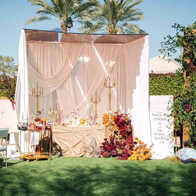 Elegant wedding table setup with draped fabric, gold candelabras, lush floral arrangements, and an interactive station featuring headphones and a writing station with ribbons.