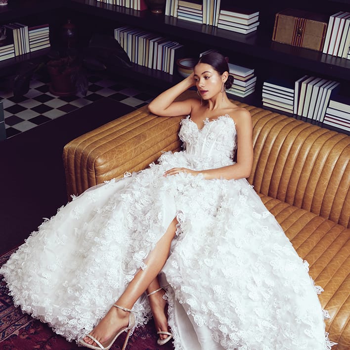 Bride lounging in library in butterfly applique Luly Yang “Butterfly Me to the Moon” gown.