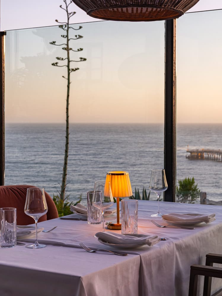 A table set for dinner overlooks the Pacific Ocean at sunset at The Ritz-Carlton Bacara, Santa Barbara, highlighting the resort’s oceanfront dining experience