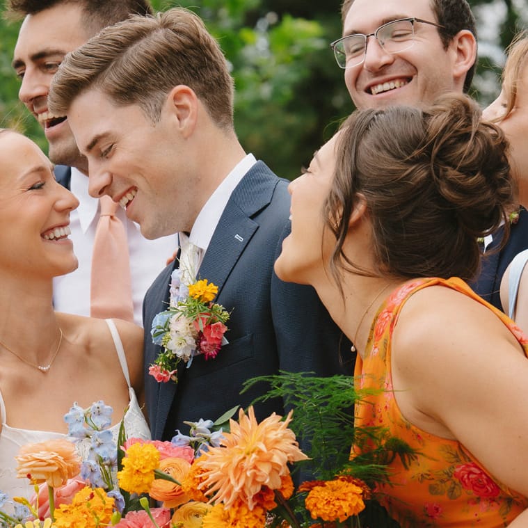 Wedding party surrounds the bride and groom as they share a loving glance