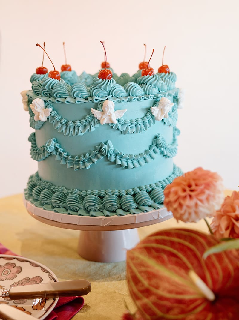 Vintage-inspired Lambeth blue wedding cake with piped details, cherubs and cherries surrounded by colorful florals and patterned tableware