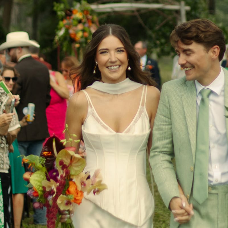 Sara and Billy smile and hold hands while they walk back down the aisle after their wedding ceremony